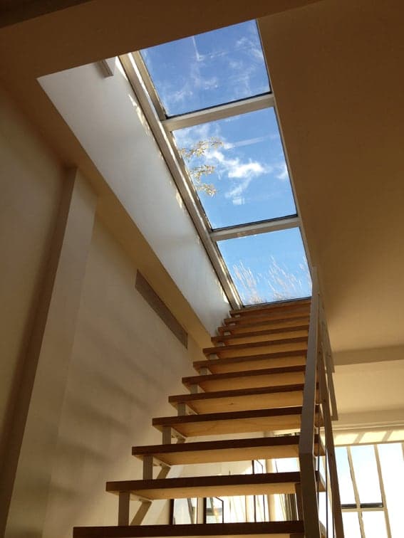 Escalier en bois montant vers un accès vitré ouvert sur le ciel
