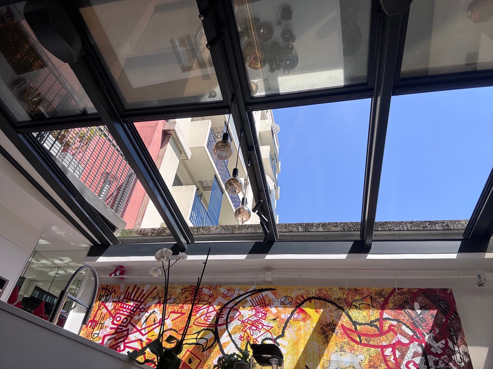 Toiture vitrée modulaire ouverte sur le ciel, au-dessus d’un séjour au mur peint