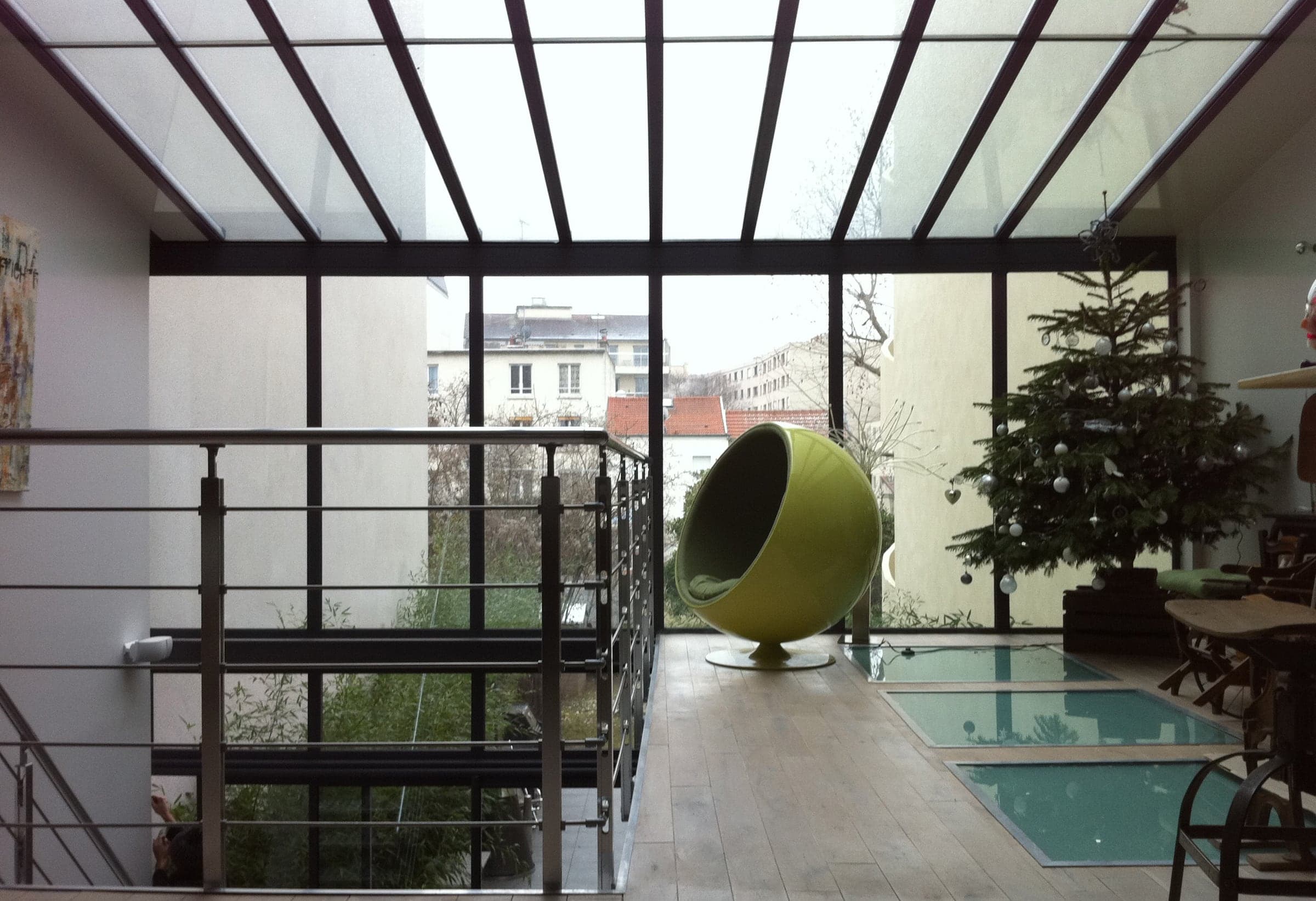 Véranda contemporaine toute vitrée ouverte sur la ville, fauteuil boule et passerelle