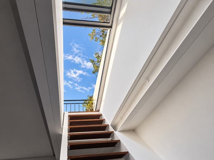 Escalier vu d’en bas vers l’accès vitré ouvert sur le ciel bleu